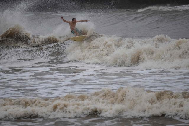 A surfer rides a high wave due to the effects of Super Typhoon Bavi in Guam on July 5, 2026. People in Guam and the Northern Marianas moved to emergency evacuation centers and made last-minute preparations on July 5, hours before a "super typhoon" was projected to bulldoze through the US Pacific territories. (Photo by Yuichi YAMAZAKI / AFP)