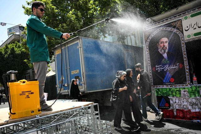 People are sprayed with water to cool off during the heat while on their way to the Grand Mosalla in Tehran on July 5, 2026, for the funeral ceremonies of Iran's slain supreme leader Ayatollah Ali Khamenei. Iranian leaders on July 5 joined prayers over the casket of late supreme leader Ali Khamenei during a second day of funeral ceremonies, which was declared a public holiday across Iran. Khamenei's body will be moved out of the Grand Mosalla later in the day, where it is lying in state, as part of preparations for processions through the capital the following day. (Photo by Ozan KOSE / AFP) / 