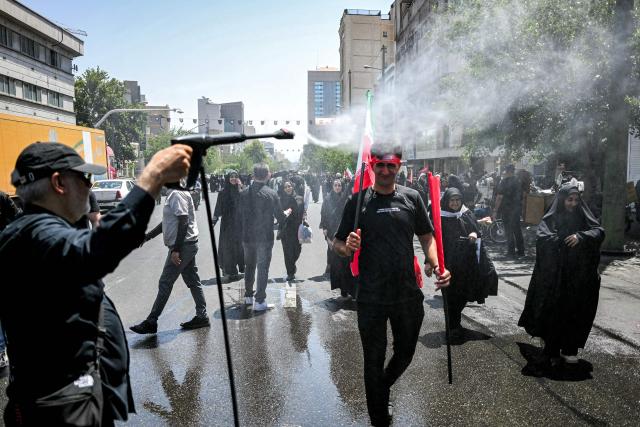 People are sprayed with water to cool off during the heat while on their way to the Grand Mosalla in Tehran on July 5, 2026, for the funeral ceremonies of Iran's slain supreme leader Ayatollah Ali Khamenei. Iranian leaders on July 5 joined prayers over the casket of late supreme leader Ali Khamenei during a second day of funeral ceremonies, which was declared a public holiday across Iran. Khamenei's body will be moved out of the Grand Mosalla later in the day, where it is lying in state, as part of preparations for processions through the capital the following day. (Photo by Ozan KOSE / AFP) / 