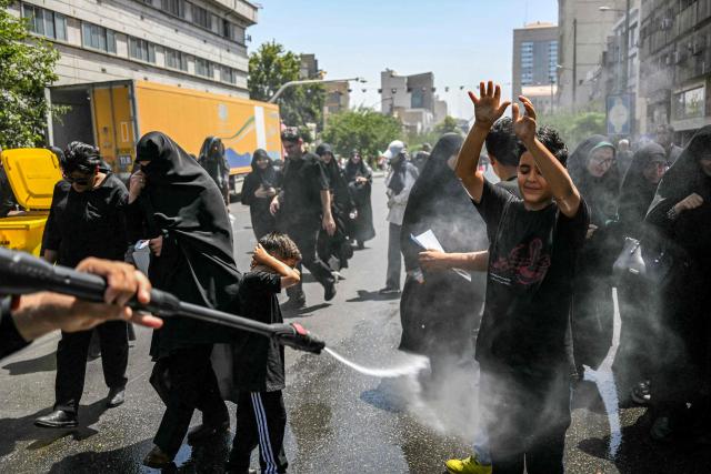 A boy reacts as he and other people are sprayed with water to cool off during the heat while on their way to the Grand Mosalla in Tehran on July 5, 2026, for the funeral ceremonies of Iran's slain supreme leader Ayatollah Ali Khamenei. Iranian leaders on July 5 joined prayers over the casket of late supreme leader Ali Khamenei during a second day of funeral ceremonies, which was declared a public holiday across Iran. Khamenei's body will be moved out of the Grand Mosalla later in the day, where it is lying in state, as part of preparations for processions through the capital the following day. (Photo by Ozan KOSE / AFP) / 