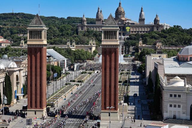 TOPSHOT - The pack of riders (peloton) cycles the Venetian Towers towards Montjuic National Palace during the 2nd stage of the 113th edition of the Tour de France cycling race, 168,5 km between Tarragona and Barcelona in northeastern Spain, on July 5, 2026. (Photo by Josep LAGO / AFP)