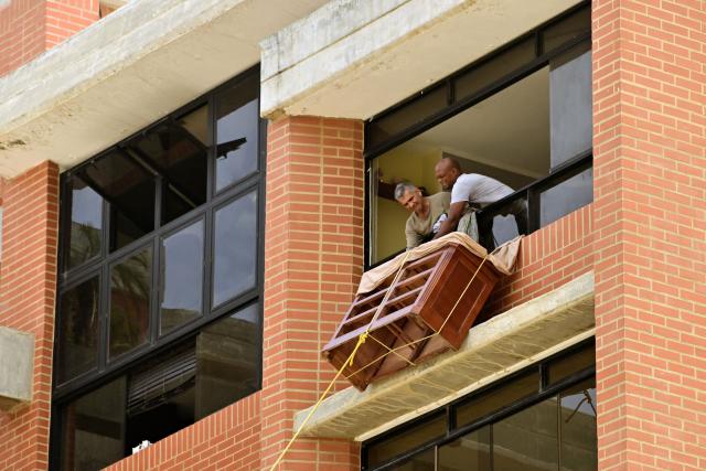 Men lower furniture through a window of a damaged building in Playa Grande, Catia La Mar, La Guaira State, Venezuela on July 5, 2026, following the June 24 twin earthquakes. The devastating earthquakes that struck Venezuela eleven days ago have now claimed nearly 3,000 lives, according to the latest figures released on July 4, 2026, as foreign rescue teams wind down their operations to find survivors. (Photo by MARTIN BERNETTI / AFP)