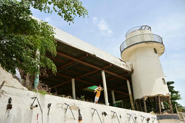 View of a lighthouse and an image of Colombia's footballer James Rodriguez in Puerto Viejo beach, Catia La Mar, La Guaira State, Venezuela on July 5, 2026, following the June 24 twin earthquakes. The devastating earthquakes that struck Venezuela eleven days ago have now claimed nearly 3,000 lives, according to the latest figures released on July 4, 2026, as foreign rescue teams wind down their operations to find survivors. (Photo by MARTIN BERNETTI / AFP)
