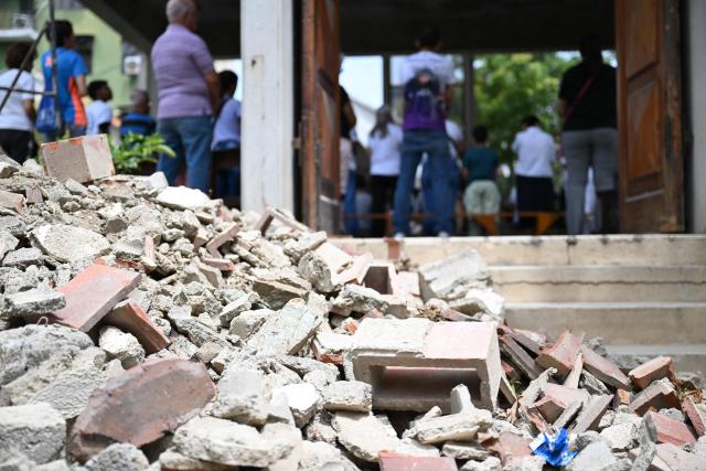 People attend a mass next to rubble at the Jerusalem square in Maiquetia, Venezuela on July 5, 2026, following the June 24 twin earthquakes. The devastating earthquakes that struck Venezuela eleven days ago have now claimed nearly 3,000 lives, according to the latest figures released on July 4, 2026, as foreign rescue teams wind down their operations to find survivors. (Photo by Raul ARBOLEDA / AFP)