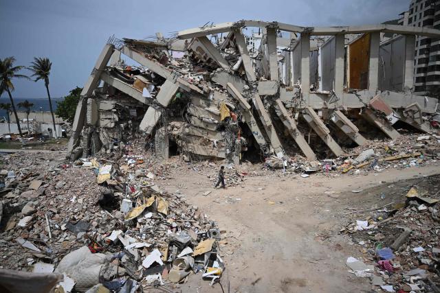 EDITORS NOTE: Graphic content / A person walks near a destroyed building in Macuto, Vargas state, Venezuela, on July 5, 2026, following the June 24 twin earthquakes. The devastating earthquakes that struck Venezuela eleven days ago have now claimed nearly 3,000 lives, according to the latest figures released on July 4, 2026, as foreign rescue teams wind down their operations to find survivors. (Photo by Raul ARBOLEDA / AFP)