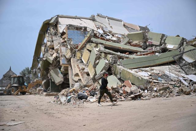 EDITORS NOTE: Graphic content / A woman walks near a destroyed building in Macuto, Vargas state, Venezuela, on July 5, 2026, following the June 24 twin earthquakes. The devastating earthquakes that struck Venezuela eleven days ago have now claimed nearly 3,000 lives, according to the latest figures released on July 4, 2026, as foreign rescue teams wind down their operations to find survivors. (Photo by Raul ARBOLEDA / AFP)