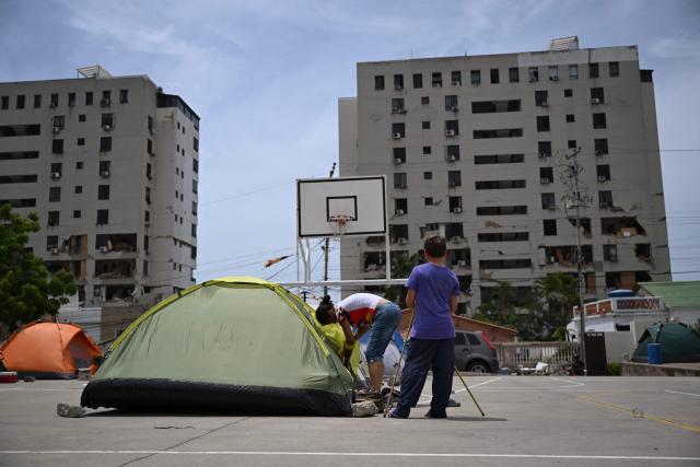 EDITORS NOTE: Graphic content / A woman and a child remain next to a tent at a makeshift camp in Macuto, Vargas state, Venezuela, on July 5, 2026, following the June 24 twin earthquakes. The devastating earthquakes that struck Venezuela eleven days ago have now claimed nearly 3,000 lives, according to the latest figures released on July 4, 2026, as foreign rescue teams wind down their operations to find survivors. (Photo by Raul ARBOLEDA / AFP)