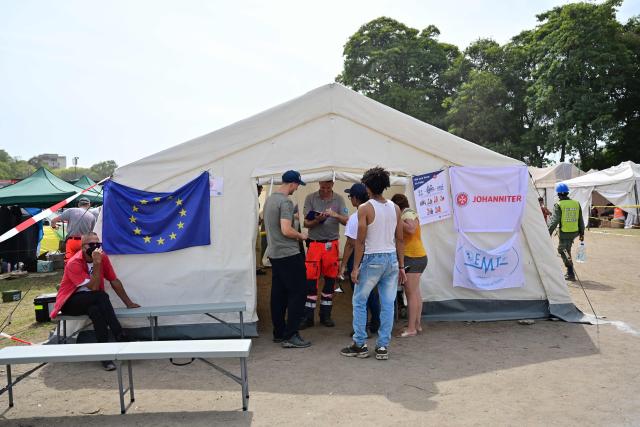 People remain outside a tent of the EU at a field hospital and refuge set up in a golf course in Caraballeda, La Guaira state, Venezuela, on July 5, 2026, following the June 24 twin earthquakes. The devastating earthquakes that struck Venezuela eleven days ago have now claimed nearly 3,000 lives, according to the latest figures released on July 4, 2026, as foreign rescue teams wind down their operations to find survivors. (Photo by MARTIN BERNETTI / AFP)