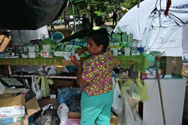 A woman distribued medicines at a field hospital and refuge set up in a golf course in Caraballeda, La Guaira state, Venezuela, on July 5, 2026, following the June 24 twin earthquakes. The devastating earthquakes that struck Venezuela eleven days ago have now claimed nearly 3,000 lives, according to the latest figures released on July 4, 2026, as foreign rescue teams wind down their operations to find survivors. (Photo by MARTIN BERNETTI / AFP)