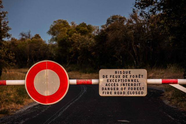 This photograph shows a roads blocked by a barrier which warns "Extreme Forest Fire Risk," near Millas, in the Pyrenees-Orientales department, southern France on July 5, 2026. A wildfire broke out on July 4 at around 19h30 (1730 GMT) in a hard-to-reach massif near Trevillach, in the Pyrenees-Orientales department of southern France and spread rapidly overnight. More than 10,000 residents are currently being evacuated as the wildfire spreads rapidly, having burned around 2,000 hectares. (Photo by Jc Milhet / AFP)