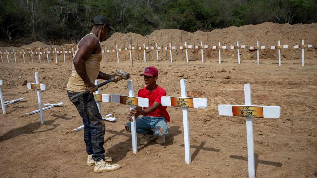 Workers nail a wooden cross onto a freshly dug grave marked with a number at La Esperanza Cemetery in Catia La Mar, La Guaira state, northeast of Caracas on July 5, 2026, where rows of similar graves for unidentified individuals, victims of twin earthquakes, stretch across the site. Venezuela's devastating twin earthquakes killed nearly 3,000, updated official figures showed on July 4, as international rescue teams began winding down search operations for survivors in the rubble of the disaster. (Photo by Miguel MEDINA / AFP)
