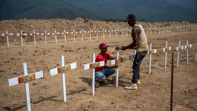 Workers nail a wooden cross onto a freshly dug grave marked with a number at La Esperanza Cemetery in Catia La Mar, La Guaira state, northeast of Caracas on July 5, 2026, where rows of similar graves for unidentified individuals, victims of twin earthquakes, stretch across the site. Venezuela's devastating twin earthquakes killed nearly 3,000, updated official figures showed on July 4, as international rescue teams began winding down search operations for survivors in the rubble of the disaster. (Photo by Miguel MEDINA / AFP)