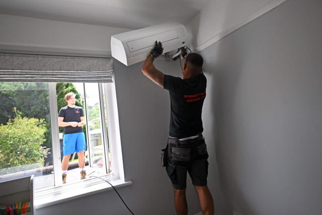 Engineers from Springett Elite Services install an air conditioning unit at a residential home in Croydon, south London, on July 1, 2026. A small but growing proportion of British households is embracing air conditioning (AC) to deal with increasingly hot summers. But the trend has attracted criticism, particularly from sustainability experts who argue it should not be the "default answer". (Photo by Justin TALLIS / AFP) / TO GO WITH Climate-weather-heatwave-Britain-airconditioning,FOCUS by Joe JACKSON