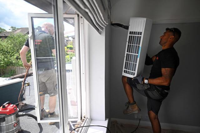 Engineers from Springett Elite Services install an air conditioning unit at a residential home in Croydon, south London, on July 1, 2026. A small but growing proportion of British households is embracing air conditioning (AC) to deal with increasingly hot summers. But the trend has attracted criticism, particularly from sustainability experts who argue it should not be the "default answer". (Photo by Justin TALLIS / AFP) / TO GO WITH Climate-weather-heatwave-Britain-airconditioning,FOCUS by Joe JACKSON