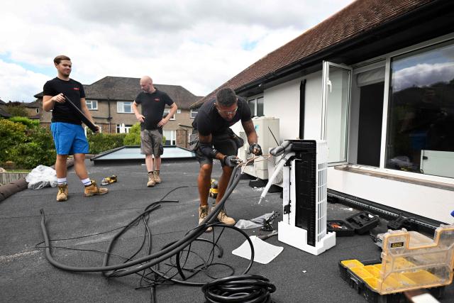 Engineers from Springett Elite Services install an air conditioning unit on the roof of a residential home in Croydon, south London, on July 1, 2026. A small but growing proportion of British households is embracing air conditioning (AC) to deal with increasingly hot summers. But the trend has attracted criticism, particularly from sustainability experts who argue it should not be the "default answer". (Photo by Justin TALLIS / AFP) / TO GO WITH Climate-weather-heatwave-Britain-airconditioning,FOCUS by Joe JACKSON