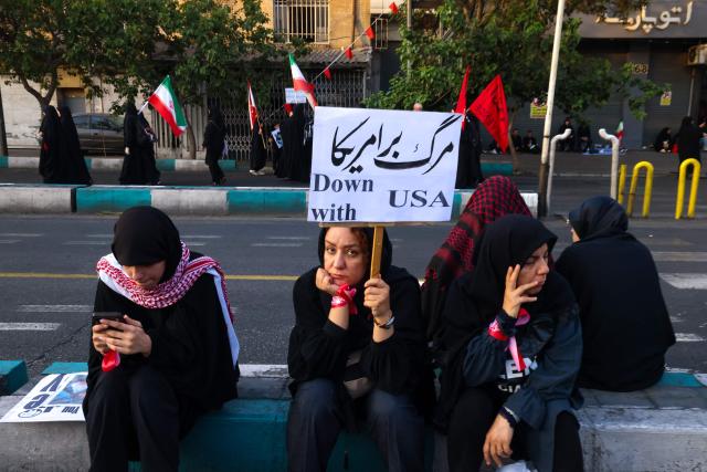 TOPSHOT - A woman holds an anti-US placard as he waits with others for the funeral procession of Iran's slain Supreme Leader Ali Khamenei in Tehran July 6, 2026. Massive crowds are expected on July 6 for the funeral procession of late Iranian supreme leader Ali Khamenei in Tehran, with authorities hoping to avoid a repeat of the chaos that accompanied his predecessor's funeral. (Photo by ATTA KENARE / AFP) / 