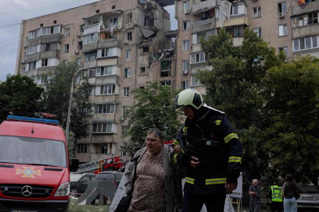 A firefighter walks with a woman near a damaged residential building following a Russian missile strike on the Ukrainian capital of Kyiv on July 6, 2026, amid the Russian invasion in Ukraine. Russia struck Ukraine's Kyiv region with ballistic missiles on July 6, killing at least eight people and wounding dozens, authorities said, on the eve of a NATO summit in Turkey. (Photo by Tetiana DZHAFAROVA / AFP)