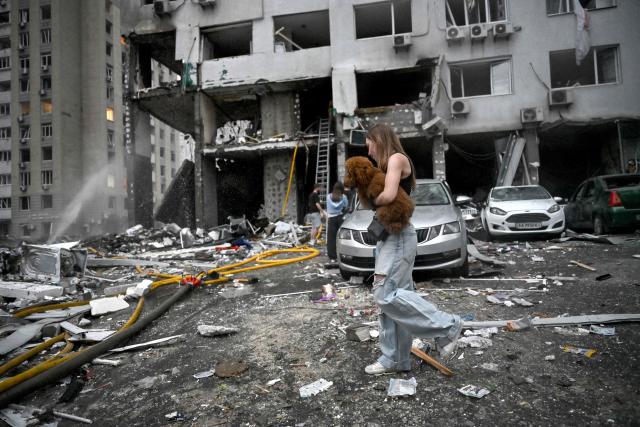 A woman carries her dog as she walks past a multistorey residential building damaged following a Russian missile strike on the Ukrainian capital of Kyiv on July 6, 2026, amid the Russian invasion in Ukraine. Russia struck Ukraine's Kyiv region with ballistic missiles on July 6, killing at least eight people and wounding dozens, authorities said, on the eve of a NATO summit in Turkey. (Photo by Genya Savilov / AFP)