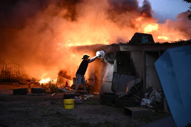 A local resident extinguishes burning garages outside a multistorey residential building damaged following a Russian missile strike on the Ukrainian capital of Kyiv on July 6, 2026, amid the Russian invasion in Ukraine. Russia struck Ukraine's Kyiv region with ballistic missiles on July 6, killing at least eight people and wounding dozens, authorities said, on the eve of a NATO summit in Turkey. (Photo by Genya Savilov / AFP)