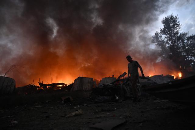 A local resident walks past burning garages outside a residential building following a Russian missile strike on the Ukrainian capital of Kyiv on July 6, 2026, amid the Russian invasion in Ukraine. Russia struck Ukraine's Kyiv region with ballistic missiles on July 6, killing at least eight people and wounding dozens, authorities said, on the eve of a NATO summit in Turkey. (Photo by Genya Savilov / AFP)