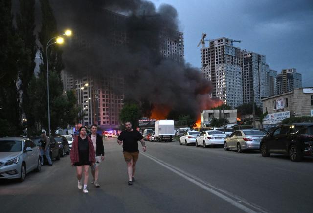Local residents walk past burning garages outside a residential building following a Russian missile strike on the Ukrainian capital of Kyiv on July 6, 2026, amid the Russian invasion in Ukraine. Russia struck Ukraine's Kyiv region with ballistic missiles on July 6, killing at least eight people and wounding dozens, authorities said, on the eve of a NATO summit in Turkey. (Photo by Genya Savilov / AFP)