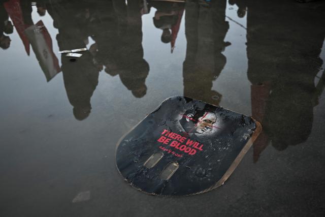 TOPSHOT - Mourners stand next to a placard calling for revenge as they gather to pay tribute to Iran's slain supreme leader Ayatollah Ali Khamenei at the Grand Mosalla on the second day of funeral ceremonies in Tehran on July 5, 2026. Prayers were held on July 5 over the casket of Iran's late supreme leader Ali Khamenei, the second day of funeral ceremonies that have drawn huge crowds to pay their final respects in Tehran. Khamenei ruled the Islamic republic from 1989 until he was killed aged 86 in an airstrike on the first day of the US-Israeli war with Iran on February 28. (Photo by Ozan KOSE / AFP) / ALTERNATIVE CROP