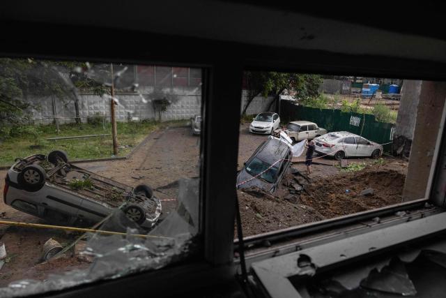 People cover a car with a plastic wrap next to a crater near a damaged residential building following a Russian missile strike on the Ukrainian capital of Kyiv on July 6, 2026, amid the Russian invasion in Ukraine. The death toll from Russian bombardment on the Kyiv region on July 6, has risen from eight to 10, authorities said, warning the number could rise further. (Photo by Tetiana DZHAFAROVA / AFP)