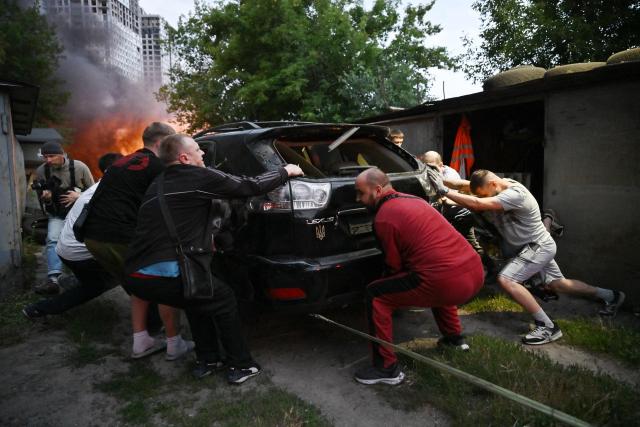 Local residents work to save a car from burning garages outside a multistorey residential building damaged following a Russian missile strike on the Ukrainian capital of Kyiv on July 6, 2026, amid the Russian invasion in Ukraine. Russia struck Kyiv's capital region with ballistic missiles on Monday, sparking fires and killing at least four people, authorities said, on the eve of a NATO summit in Ankara. (Photo by Genya Savilov / AFP)
