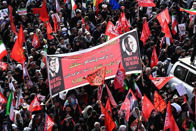People hold a banner depicting US President Donald Trump and Israel's Prime Minister Benjamin Netanyahu displaying the words "There Will Be Blood" as they gather along a street for the funeral procession of Iran's slain Supreme Leader Ali Khamenei in Tehran July 6, 2026. The funeral procession for Iran's late supreme leader Ali Khamenei began in Tehran on July 6, state television reported, as authorities prepared for crowds that could rival those that turned out for his predecessor nearly four decades ago. (Photo by Wakil Kohsar / AFP) / 