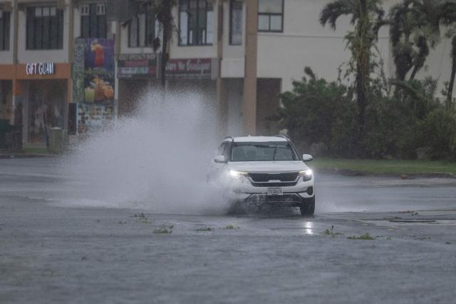 A car drives through a flooded road after heavy rain brought by Super Typhoon Bavi in Guam on July 6, 2026. A "super typhoon" with the force of a category-five hurricane tore through the US Pacific territories of Northern Marianas and Guam on July 6, with authorities saying they had received reports of "major" damage on the small island of Rota. (Photo by Yuichi YAMAZAKI / AFP)