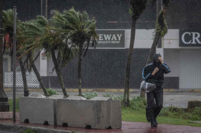 A pedestrian walks through heavy rain and strong winds brought by Super Typhoon Bavi in Guam on July 6, 2026. A "super typhoon" with the force of a category-five hurricane tore through the US Pacific territories of Northern Marianas and Guam on July 6, with authorities saying they had received reports of "major" damage on the small island of Rota. (Photo by Yuichi YAMAZAKI / AFP)
