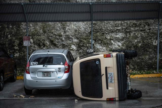 A car lies overturned after being flipped by strong winds brought by Super Typhoon Bavi in Guam on July 6, 2026. A "super typhoon" with the force of a category-five hurricane tore through the US Pacific territories of Northern Marianas and Guam on July 6, with authorities saying they had received reports of "major" damage on the small island of Rota. (Photo by Yuichi YAMAZAKI / AFP)