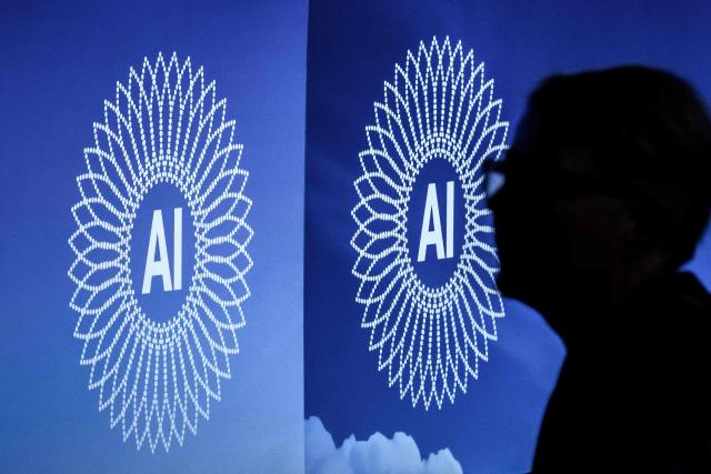 A person is silhouetted next to the logo of the first Global Dialogue on AI Governance, in Geneva on July 6, 2026. Guterres called for a global governance system to shape artificial intelligence for the good of humanity, warning against allowing the technology itself to "vibe-code" our future.  (Photo by Fabrice COFFRINI / AFP)