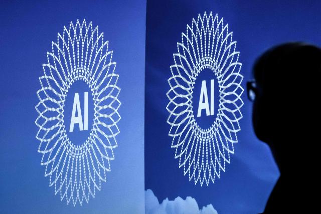 A person is silhouetted next to the logo of the first Global Dialogue on AI Governance, in Geneva on July 6, 2026. Guterres called for a global governance system to shape artificial intelligence for the good of humanity, warning against allowing the technology itself to "vibe-code" our future.  (Photo by Fabrice COFFRINI / AFP)