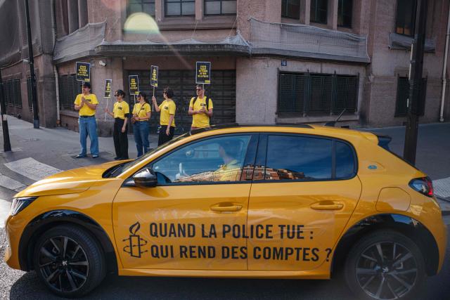 An activist takes part in a car displaying the message 'When the police kill, who is held accountable' during a symbolic action by Amnesty International against the criminal justice and victim respect bill at the Ministry of the Interior branch in Paris on July 6, 2026. The bill on the presumption of self-defense for law enforcement, which is due to be debated on July 7, 2026 at the National Assembly, risks creating a "license to kill" and a form of blanket immunity for police officers and gendarmes, human rights defenders warn. (Photo by Dimitar DILKOFF / AFP)