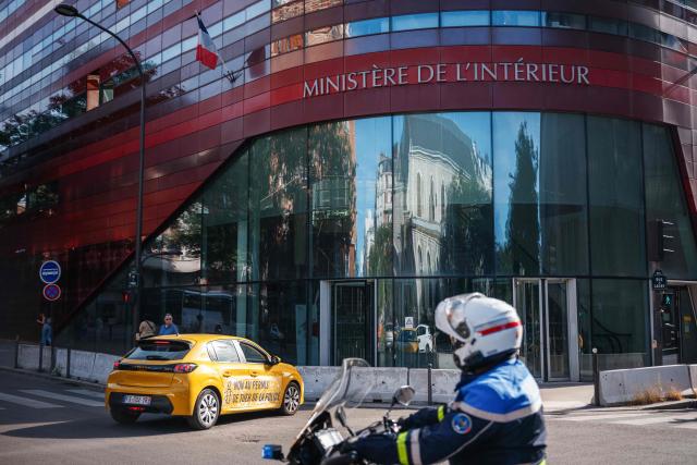 A police motorcyclist looks at an activist taking part in a car displaying the message 'No to the police's license to kill' in a symbolic action by Amnesty International against the criminal justice and victim respect bill at the Ministry of the Interior branch in Paris on July 6, 2026. The bill on the presumption of self-defense for law enforcement, which is due to be debated on July 7, 2026 at the National Assembly, risks creating a "license to kill" and a form of blanket immunity for police officers and gendarmes, human rights defenders warn. (Photo by Dimitar DILKOFF / AFP)