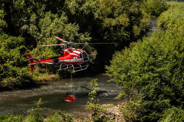 A water-bombing helicopter takes on water from the River Tet in the town of Ille sur Tet as a wildfire rages in the southern France department of Pyrenees-Orientales where 700 hundred firefighters backed by special aircraft battled to control a "gigantic" blaze spreading in a hard-to-reach remote area, with more than 10,000 local residents evacuated, near Perpignan on July 6, 2026. Wildfires raged across southern Europe, forcing thousands of people to evacuate their homes and prompting officials to ban spectators from a stage of the storied Tour de France cycling race. (Photo by Jean-Christophe MILHET / AFP)