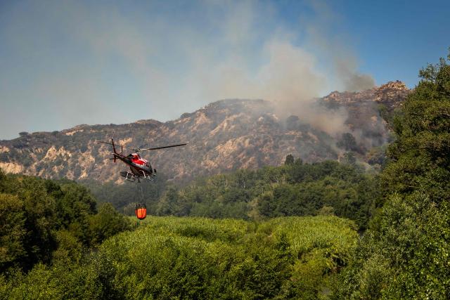 A water-bombing helicopter heads towards a flare-up of the fire in the town of Ille sur Tet as a wildfire rages in the southern France department of Pyrenees-Orientales where 700 hundred firefighters backed by special aircraft battled to control a "gigantic" blaze spreading in a hard-to-reach remote area, with more than 10,000 local residents evacuated, near Perpignan on July 6, 2026. Wildfires raged across southern Europe, forcing thousands of people to evacuate their homes and prompting officials to ban spectators from a stage of the storied Tour de France cycling race. (Photo by Jc Milhet / AFP)