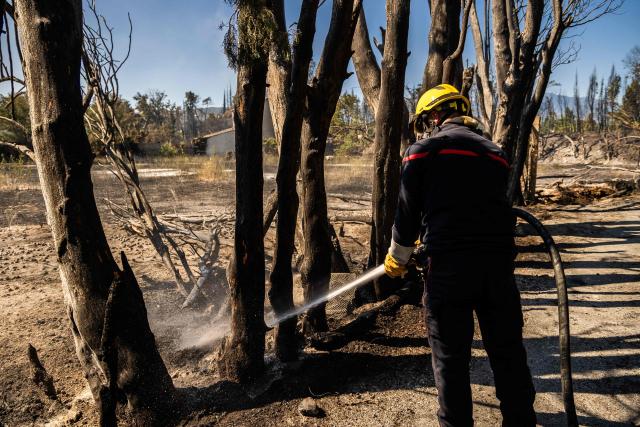A firefighter sprays water on smoke plumes to prevent the fire from reigniting in the town of Ille sur Tet as a wildfire rages in the southern France department of Pyrenees-Orientales where 700 hundred firefighters backed by special aircraft battled to control a "gigantic" blaze spreading in a hard-to-reach remote area, with more than 10,000 local residents evacuated, near Perpignan on July 6, 2026. Wildfires raged across southern Europe, forcing thousands of people to evacuate their homes and prompting officials to ban spectators from a stage of the storied Tour de France cycling race. (Photo by Jean-Christophe MILHET / AFP)