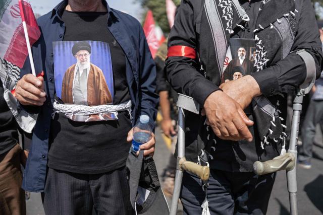 A mourner wears a T-shirt bearing the portrait of Iran's slain supreme leader Ayatollah Ali Khamenei as people attend his funeral procession and that of members of his family, along a street in Tehran on July 6, 2026. Vast crowds gathered for the funeral procession of Iran's slain supreme leader Ali Khamenei in Tehran on July 6, with authorities estimating millions were on the streets in numbers that could rival those of his predecessor's farewell nearly four decades ago. (Photo by AFP) / 