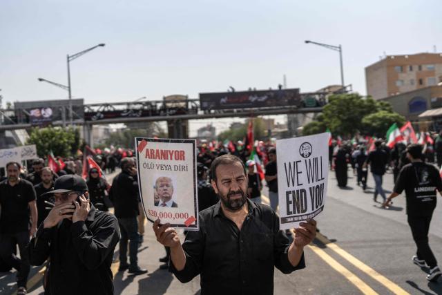 A mourner holds placards with anti-US slogans as people attend the funeral pocession of Iran's slain supreme leader Ayatollah Ali Khamenei and his family members in Tehran on July 6, 2026. Vast crowds gathered for the funeral procession of Iran's slain supreme leader Ali Khamenei in Tehran on July 6, with authorities estimating millions were on the streets in numbers that could rival those of his predecessor's farewell nearly four decades ago. (Photo by AFP) / 