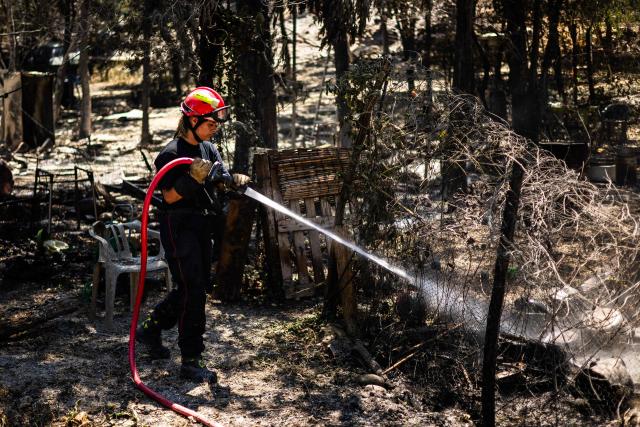 A firefighter sprays water on smoke plumes to prevent the fire from reigniting as a wildfire rages in the southern France department of Pyrenees-Orientales in the town of Ille-sur-Tet, near Perpignan on July 6, 2026. 700 firefighters backed by special aircraft battled to control a "gigantic" blaze spreading in a hard-to-reach remote area near Ille-sur-Tet. Wildfires raged across southern Europe, forcing thousands of people to evacuate their homes and prompting officials to ban spectators from a stage of the storied Tour de France cycling race. (Photo by Jean-Christophe MILHET / AFP)