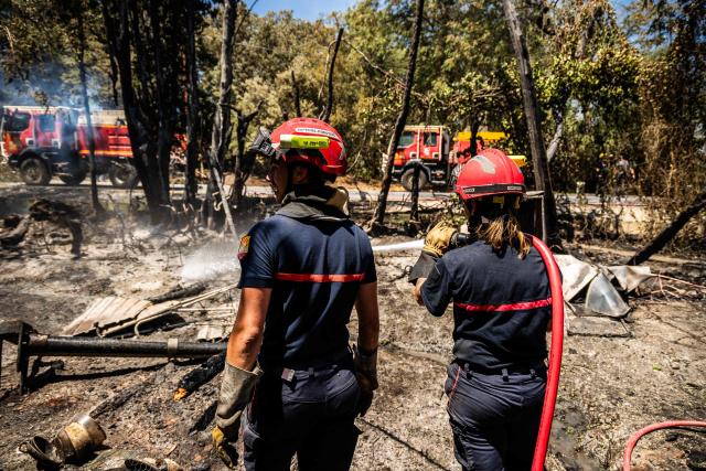 A firefighter sprays water on smoke plumes to prevent the fire from reigniting as a wildfire rages in the southern France department of Pyrenees-Orientales in the town of Ille-sur-Tet, near Perpignan on July 6, 2026. 700 firefighters backed by special aircraft battled to control a "gigantic" blaze spreading in a hard-to-reach remote area near Ille-sur-Tet. Wildfires raged across southern Europe, forcing thousands of people to evacuate their homes and prompting officials to ban spectators from a stage of the storied Tour de France cycling race. (Photo by Jc Milhet / AFP)