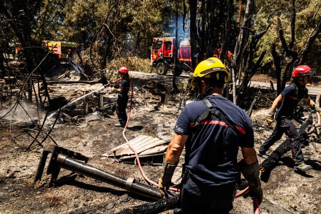 A firefighter sprays water on smoke plumes to prevent the fire from reigniting as a wildfire rages in the southern France department of Pyrenees-Orientales in the town of Ille-sur-Tet, near Perpignan on July 6, 2026. 700 firefighters backed by special aircraft battled to control a "gigantic" blaze spreading in a hard-to-reach remote area near Ille-sur-Tet. Wildfires raged across southern Europe, forcing thousands of people to evacuate their homes and prompting officials to ban spectators from a stage of the storied Tour de France cycling race. (Photo by Jc Milhet / AFP)
