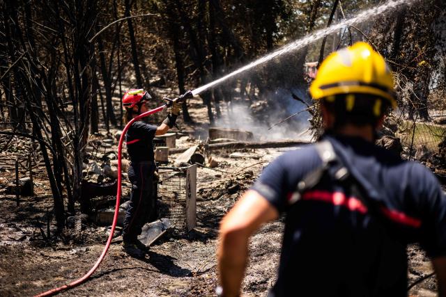 A firefighter sprays water on smoke plumes to prevent the fire from reigniting as a wildfire rages in the southern France department of Pyrenees-Orientales in the town of Ille-sur-Tet, near Perpignan on July 6, 2026. 700 firefighters backed by special aircraft battled to control a "gigantic" blaze spreading in a hard-to-reach remote area near Ille-sur-Tet. Wildfires raged across southern Europe, forcing thousands of people to evacuate their homes and prompting officials to ban spectators from a stage of the storied Tour de France cycling race. (Photo by Jean-Christophe MILHET / AFP)
