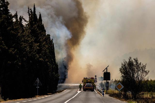 A firefighter sprays water on flames as a wildfire rages in the southern France department of Pyrenees-Orientales near the town of Bouleternere, near Perpignan on July 6, 2026. 700 firefighters backed by special aircraft battled to control a "gigantic" blaze spreading in a hard-to-reach remote area near Ille-sur-Tet. Wildfires raged across southern Europe, forcing thousands of people to evacuate their homes and prompting officials to ban spectators from a stage of the storied Tour de France cycling race. (Photo by Jc Milhet / AFP)
