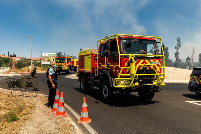 French gendarmes watch firefighters vehicles heading to the site where a wildfire rages in the southern France department of Pyrenees-Orientales near the town of Bouleternere, near Perpignan on July 6, 2026. 700 firefighters backed by special aircraft battled to control a "gigantic" blaze spreading in a hard-to-reach remote area near Ille-sur-Tet. Wildfires raged across southern Europe, forcing thousands of people to evacuate their homes and prompting officials to ban spectators from a stage of the storied Tour de France cycling race. (Photo by Jean-Christophe MILHET / AFP)