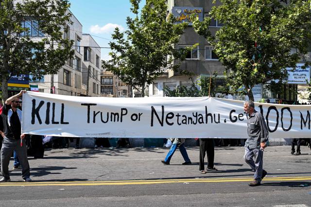 Mourners hold up a large banner urging a reward for revenge against US President Donald Trump and Israeli Prime Minister Benjamin Netanyahu during a funerary procession for Iran's slain supreme leader Ali Khamenei and his family members near Azadi Square in Tehran on July 6, 2026. Massive crowds are expected on July 6 for the funeral procession of late Iranian supreme leader Ali Khamenei in Tehran, with authorities hoping to avoid a repeat of the chaos that accompanied his predecessor's funeral. (Photo by Wakil Kohsar / AFP) / 