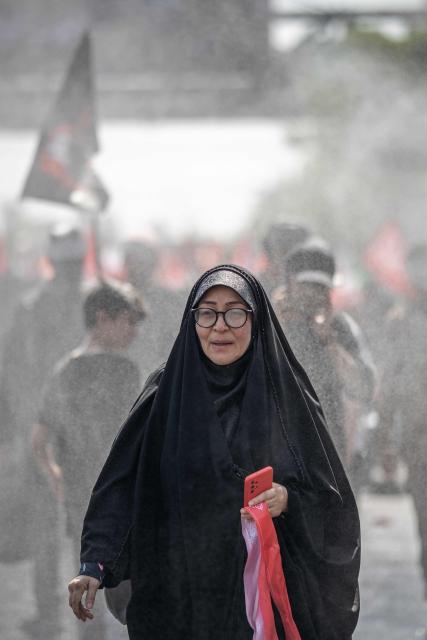 A mourner walks through the sprays of water as she attends the funeral procession of Iran's slain supreme leader Ali Khamenei and his family members, along a street in Tehran July 6, 2026. Vast crowds gathered for the funeral procession of Iran's slain supreme leader Ali Khamenei in Tehran on July 6, with authorities estimating millions were on the streets in numbers that could rival those of his predecessor's farewell nearly four decades ago. (Photo by AFP) / 