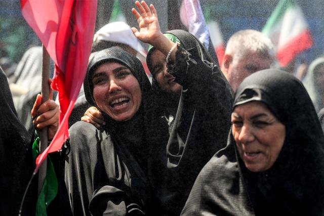Women and a girl react as they are sprayed with water to cool off as they march with other mourners towards Azadi Square in Tehran on July 6, 2026 during a funeral procession for Iran's slain supreme leader Ali Khamenei and his family members. Massive crowds are expected on July 6 for the funeral procession of late Iranian supreme leader Ali Khamenei in Tehran, with authorities hoping to avoid a repeat of the chaos that accompanied his predecessor's funeral. (Photo by Wakil Kohsar / AFP) / 